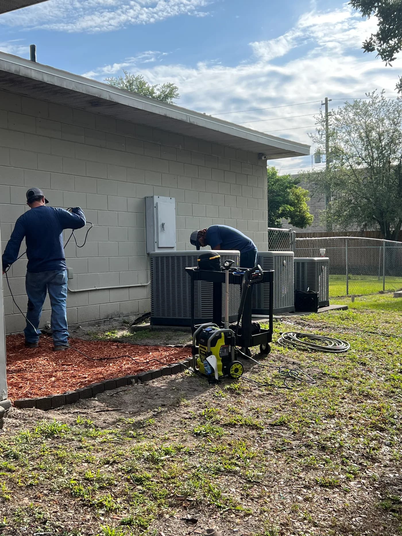 Two Blue Works technicians servicing multiple commercial split-system condenser units