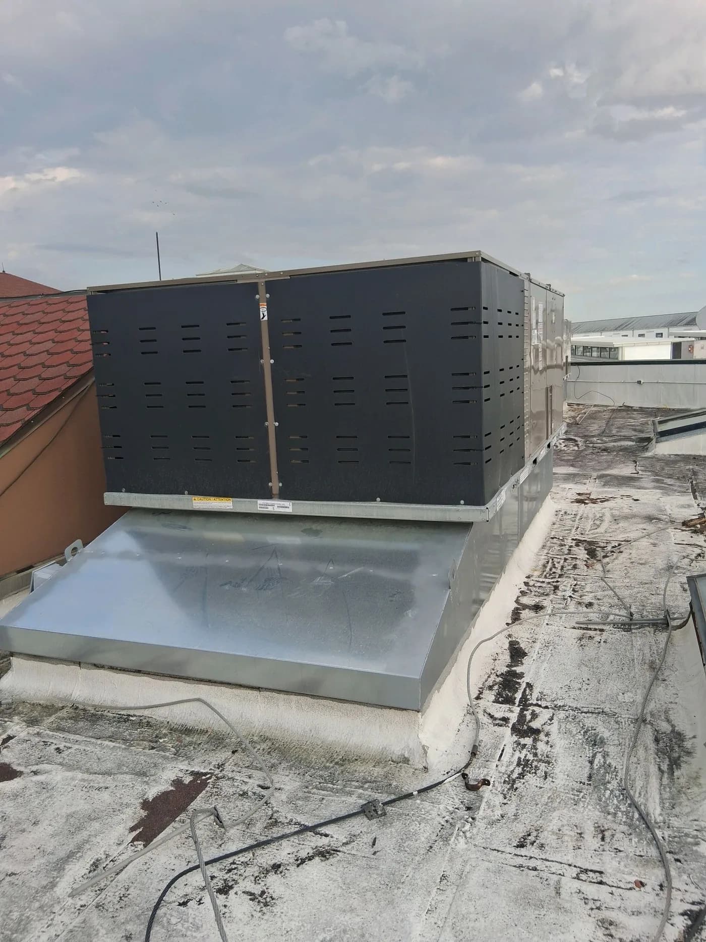 Commercial rooftop HVAC unit mounted on a galvanized curb with roof flashing and sealant